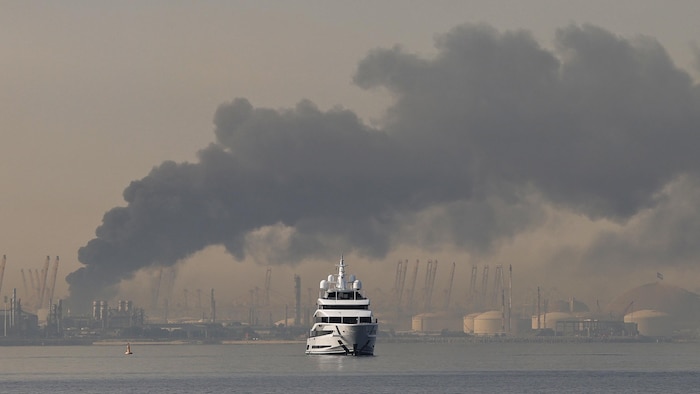 Un yacht passe devant un panache de fumée s'élevant du port de Jebel Ali après une frappe iranienne signalée à Dubaï le 1er mars 2026.