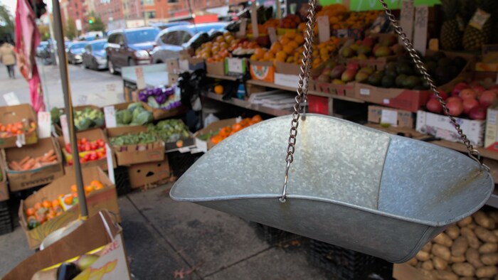 Une balance en métal devant des boîtes contenant divers fruits et légumes, protégés par une tente en toile. 