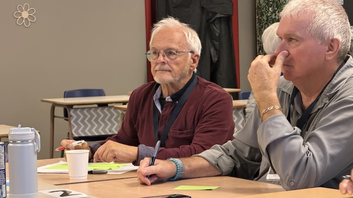 Deux hommes âgés portant des lunettes sont assises à une table en bois.