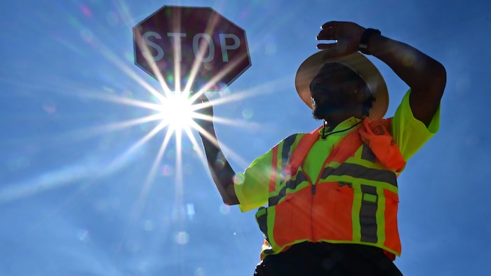 Un homme tient un panneau d'arrêt sous un soleil de plomb.