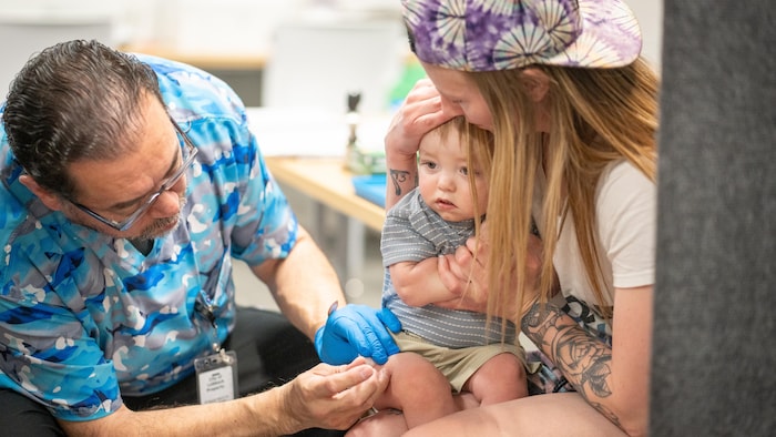 Un petit enfant, assis sur les genoux de sa mère, se fait vacciner contre la rougeole.