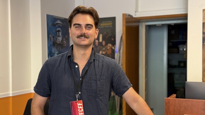 Ethan Hickey, directeur général du Forest City Film Festival, debout derrière un comptoir, portant un laissez-passer du festival autour du cou.