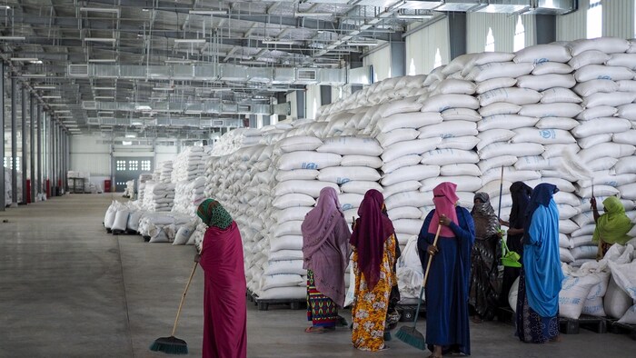 Des femmes balaient le plancher d'un entrepôt rempli de sacs de blé du Programme alimentaire mondial.