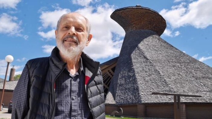 Un homme pose devant une église au toit de bois.
