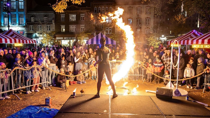 Une artiste crache du feu sur scène devant un public attentif réuni de nuit lors d’un festival.