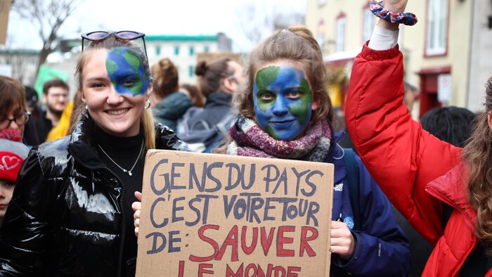 Deux adolescentes avec le visage peint en planète terre montrent leur pancarte dans une manifestation à Québec. 