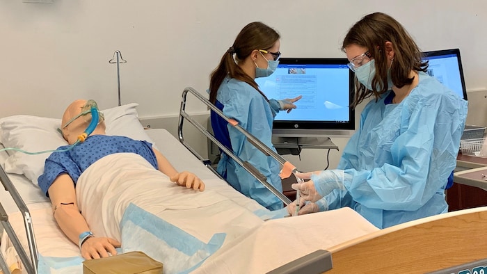Deux étudiants en soins infirmiers portant des masques médicaux travaillent avec un mannequin sur un lit d'hôpital.