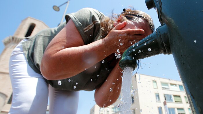 Une femme s'asperge le visage d'eau.