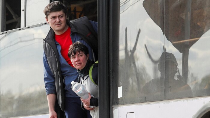 Un homme et une femme debout sur les marches dans l'entrebâillement de la porte d'un autobus. 