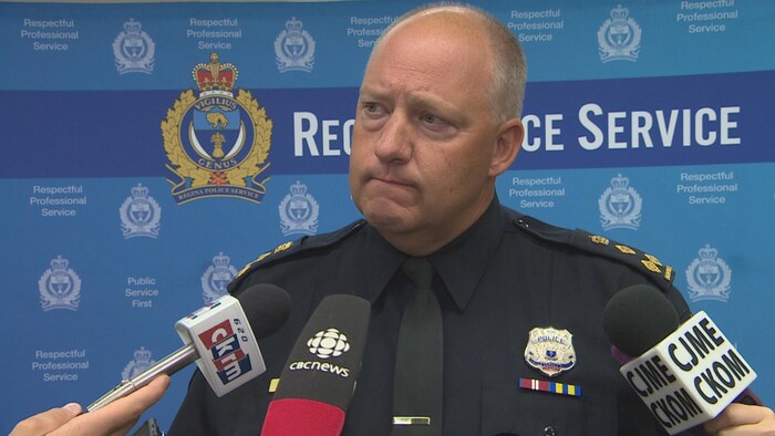 Evan Bray parle aux journalistes devant un panneau de la police de Regina bleu.