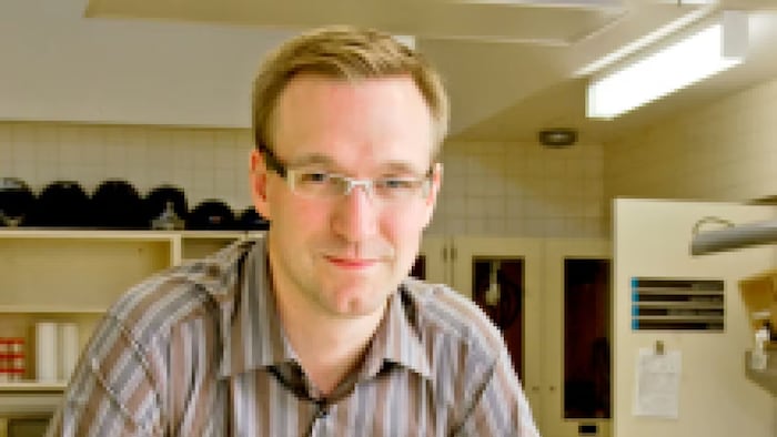 Un homme portant des lunettes fixe du regard l'objectif d'une caméra.