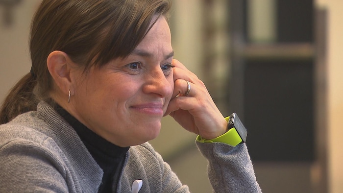 Une femme souriante avec la tête appuyé sur sa main gauche.