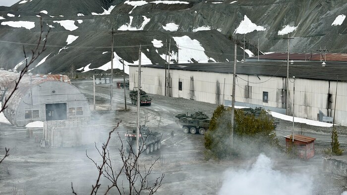 Des véhicules blindés circulent près d’un bâtiment lors d’un exercice militaire qui se déroule dans une mine. À l’avant-plan, un écran de fumée blanche provoqué par une bombe fumigène. 
