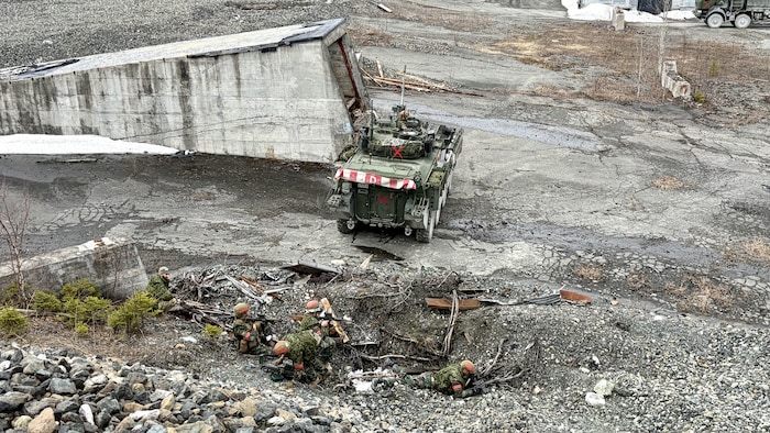 Des militaires se tiennent dans une tranchée improvisée lors d’un exercice. Près d’eux, un véhicule blindé à chenilles.