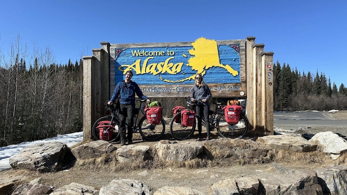 Ils posent avec leurs vélos devant une grande enseigne «Welcome to Alaska».