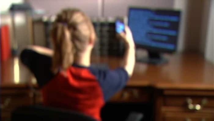 Une adolescente soulève son chandail devant un écran d'ordinateur.