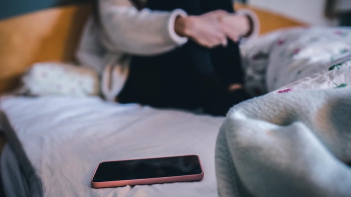 Un téléphone cellulaire sur le lit d'une jeune femme.