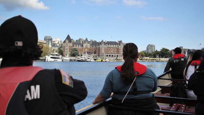 Des personnes dans un canoë avec au loin un hôtel et des bateaux.