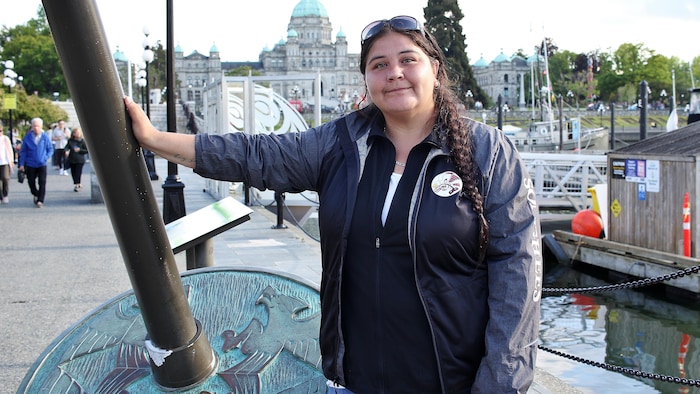 Melissa McClurg pose sa main sur la sculpture d'une fusaïole, avec en arrière-plan l'Assemblée législative