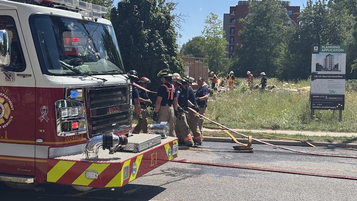 Un camion du Service des incendies de London est stationné devant les débris de la résidence. Des pompiers travaillent sur le site, près d'une affiche annonçant un projet d'aménagement.