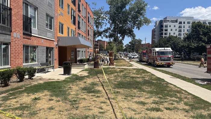 Des camions du Service des incendies de London et des voitures de police sont stationnés sur Base Line Road West. Des pompiers travaillent près des débris de la résidence détruite.
