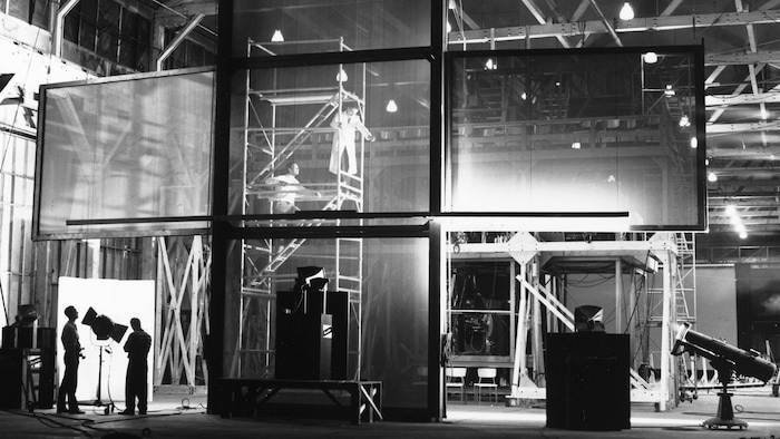 Des ouvriers en train d'installer un écran en forme de croix, dans un pavillon en construction d'Expo 67.
