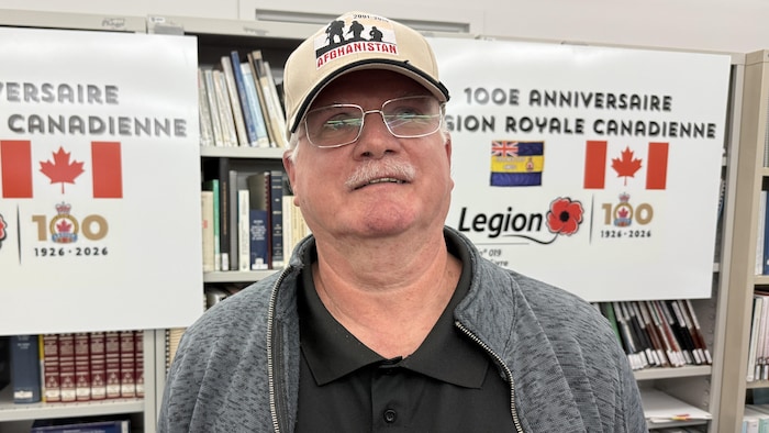 Jean Guillemet pose devant des affiches du 100e anniversaire de la Légion royale canadienne.