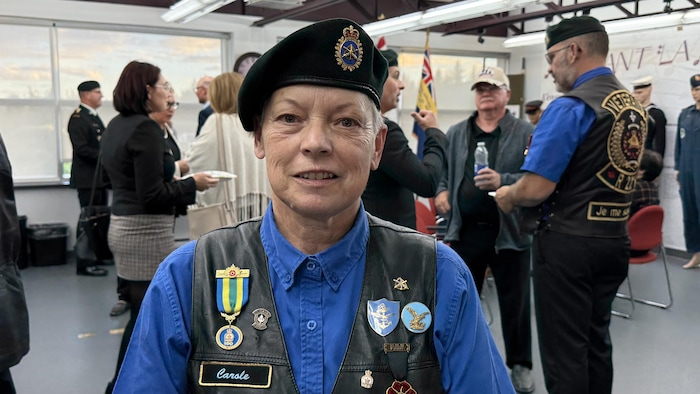Carole Nault pose avec une veste, un béret et des décorations militaires dans une salle d'exposition.