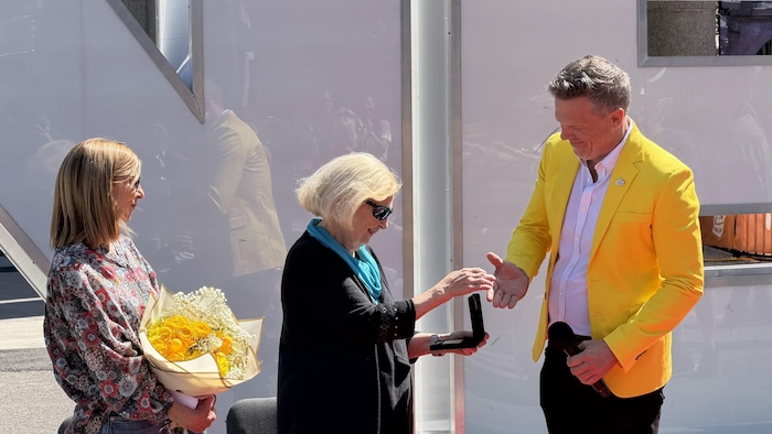 Mark Holland présente le Billet d'or à Barbara Batten Mitchell pendant qu'Elaine Darwin tient un bouquet.