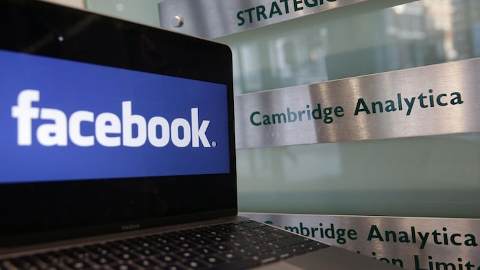 Un ordinateur portable montrant le logo de Facebook est posé à côté d'une plaque indiquant les bureaux de Cambridge Analytica.