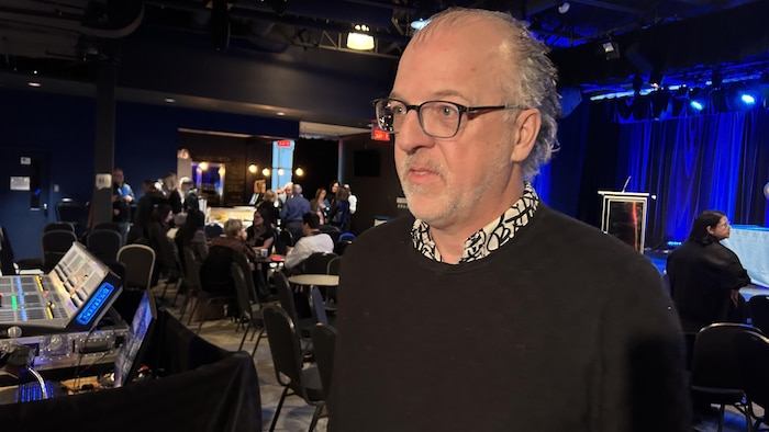 Patrice St-Pierre discute dans une salle avec des gens assis derrière lui.