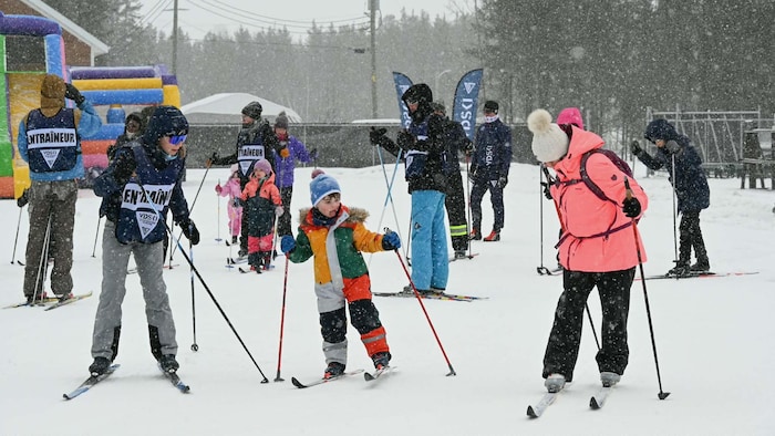 Des enfants et des adultes en skis de fond pendant que la neige tombe.