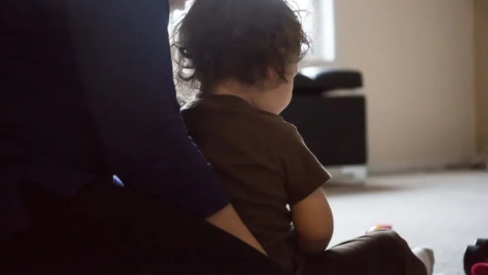 A toddler leaning against an adult, both sitting on the floor with their back to the camera.