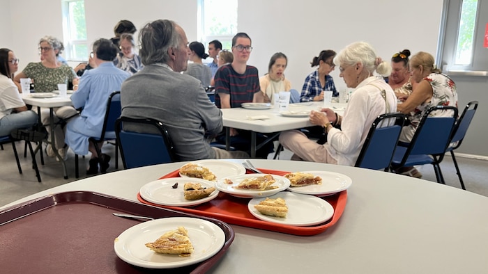 Des pointes de tartes dans des assiettes sur des plateaux. Des gens mangent un repas ensemble dans une grande salle.