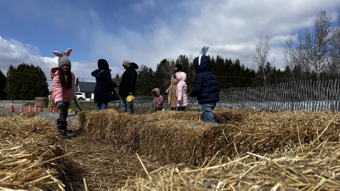 Des enfants sont debout dans les balles de foin. Deux petits portent des oreilles de lapin.