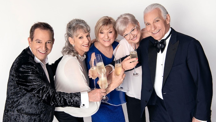Deux hommes et trois femmes sont tout sourire, verre de champagne en main, sur fond blanc. 