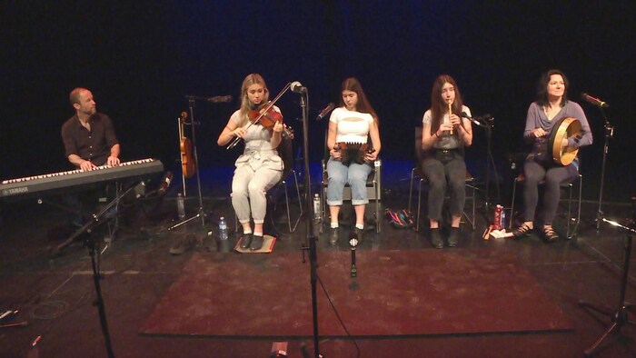 Un homme au clavier, trois adolescentes au violon, à l'accordéon et à la flûte, et une femme adulte avec un tambourin.