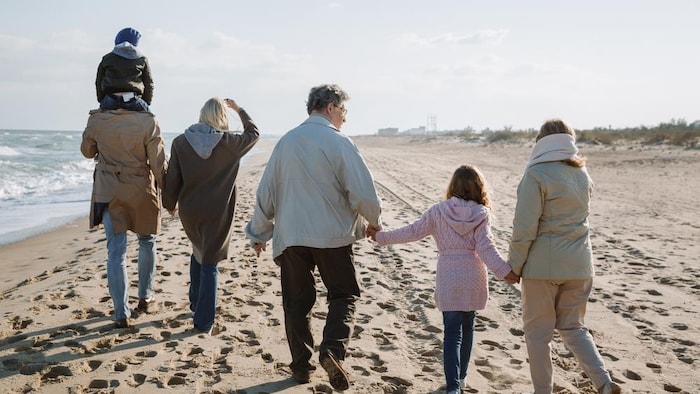Une famille multigénérationnelle marchant ensemble au bord de la mer.