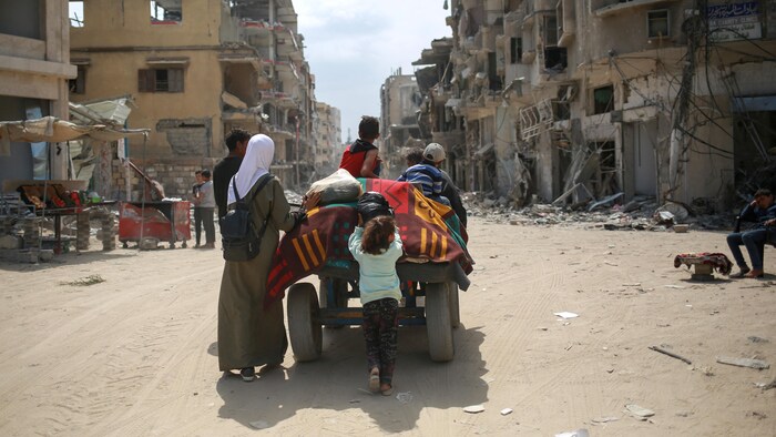 Une famille marche à côté d'un chariot dans une rue bordée par des immeubles en ruine.