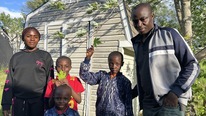 Les cinq membres de la famille Pefedieu posent pour la photo devant un cabanon. Deux des garçons tiennent des feuilles d'érable en symbole de leur terre d'accueil. 