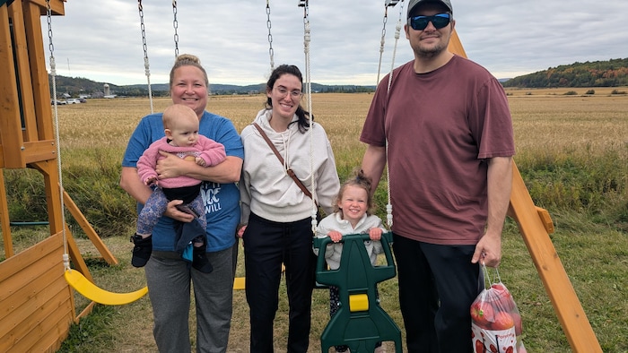 Shanon Benoit tient un bébé dans ses bras et posent à côté des parents, qui tiennent leur autre enfant dans une balançoire.