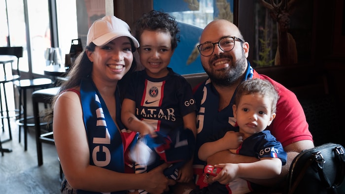 Une famille, avec des écharpes et des maillots du PSG, regarde à la caméra.