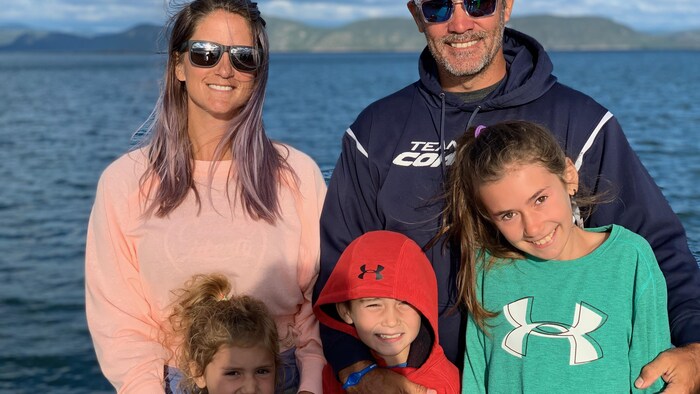 Les parents et leurs trois enfants prennent la pose sur le bord de l'eau, cheveux au vent.