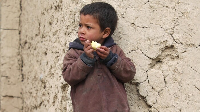 Un garçon mange une pomme, près d'un mur.
