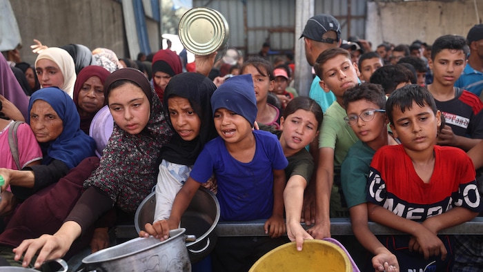 Des enfants tendent des récipients pour recevoir de la nourriture.