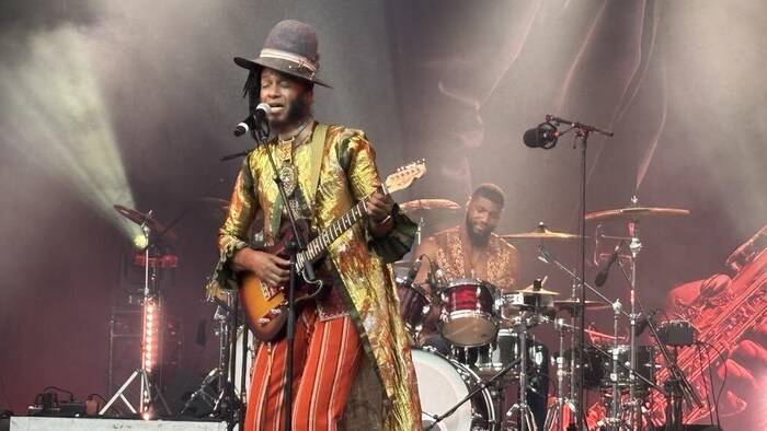 Un homme à la guitare devant un micro, avec derrière lui un batteur.