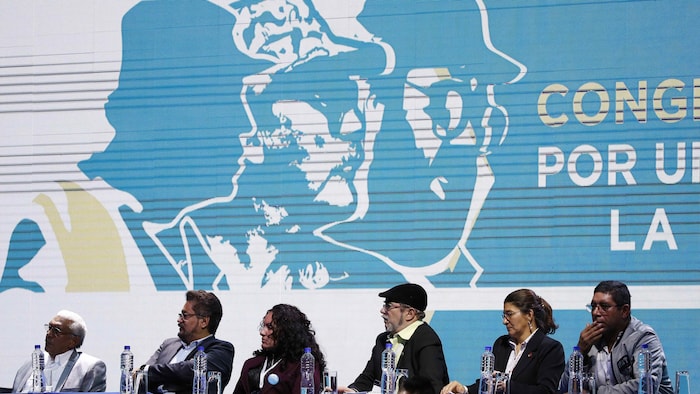 Les dirigeants de la FARC en congrès national à Bogota, assis côte à côte devant une énorme affiche blanche et bleue.