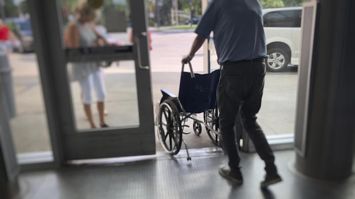Un homme pousse un fauteuil roulant en passant la porte.