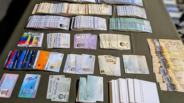 Des permis de conduire, des billets de 100 $, des cartes de crédit tous faux sont disposés sur une table. 