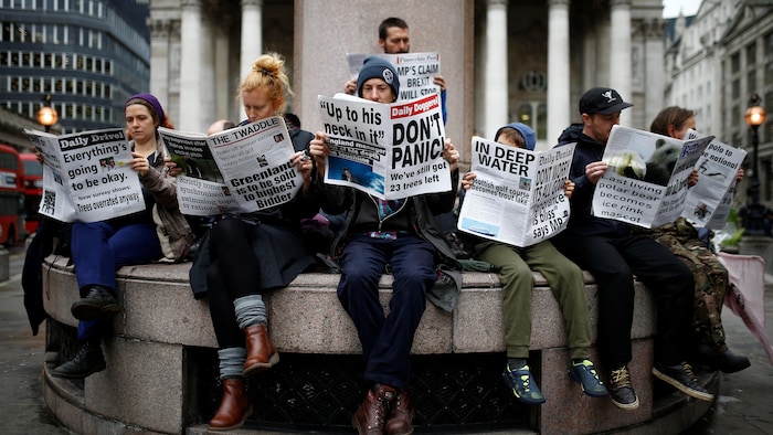 Des gens sont assis et lisent de faux journaux satiriques avec des titres comme « Don't Panic ».